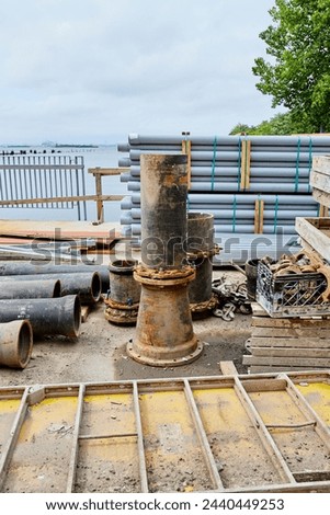 Large Iron Pipe on End next to Stack of PVC Tubes