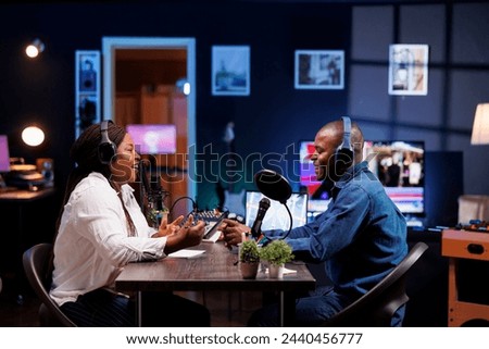 Cheerful african american couple having a conversation at home, and using audio equipment for podcast episode. Joyful male and female influencers wearing wireless headphones and talking into mics.