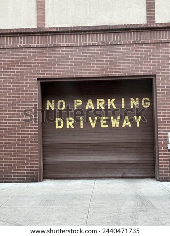 No parking sign in yellow on a brown gate or entrance of a brown brick building and grey sidewalks