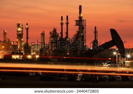 Evening traffic passes by an oil pump jack and refinery in Bakersfield, California, USA at sunset.