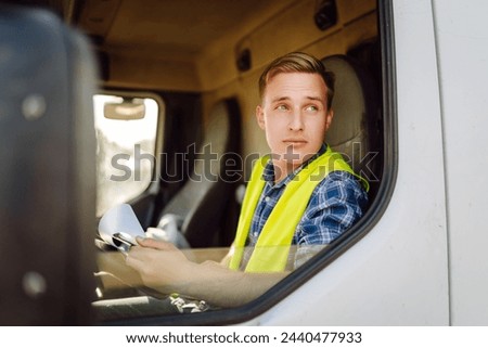 Truck driver job. Logistics - proud driver or forwarder on truck and trailer, on a transshipment point. Transportation service. Royalty-Free Stock Photo #2440477933