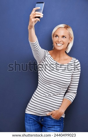 Happy woman, selfie and fashion with phone for photography, picture or moment on a blue studio background. Female person, blonde or model with smile for photo, memory or social media on mockup space
