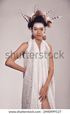 Model, portrait or culture headdress in studio with feathers, fashion and tribal make up in trendy clothes. Native american woman, face and indigenous cosmetics in robe and elegant on grey background