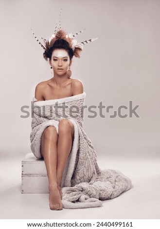 Woman, fashion and native american headdress in studio with feathers in hair, portrait and culture make up in modern blanket. Model, face and indigenous on box and elegant cloth on grey background