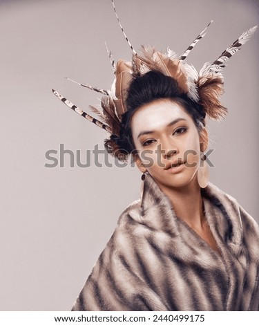 Woman, portrait and cultural fashion with Native American in tradition or art on a gray studio background. Female person with feather, face paint or stylish tribal clothing of goddess in beauty