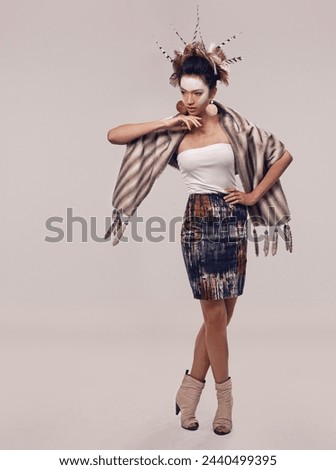 Model, dancer or culture headdress in studio with feathers, fashion and tribal make up in trendy clothes. Native american woman, creative and indigenous cosmetics and accessories on grey background
