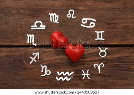 Zodiac signs and red hearts on wooden background, flat lay