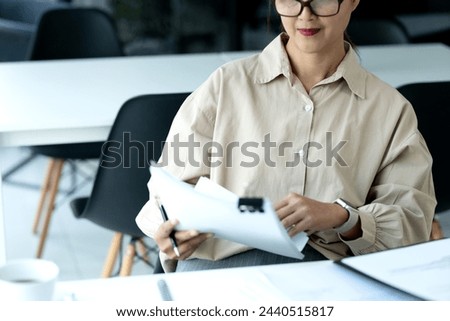 Middle-aged businesswoman  was sitting and looking at the piles of information recorded on paper on a desk full of documents with the intention of working slowly.