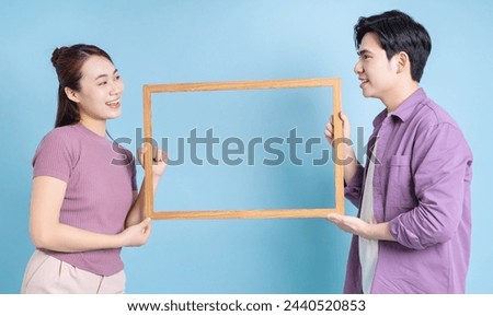 Young Asian couple holding photo frame on blue background