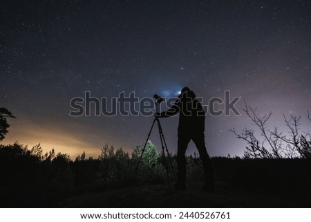 Landscape astrophotographer with a camera on a tripod outdoors in early spring at night under the starry sky.  Royalty-Free Stock Photo #2440526761