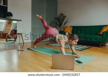 Woman in sportswear doing yoga on hardwood flooring in front of a laptop