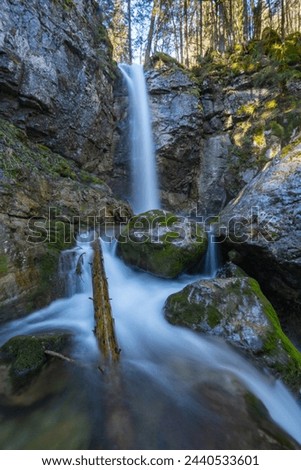 The Sibli waterfall which flows into the Rottach (in Bavaria near Lake Tegernsee). The water falls a few meters down the rock and runs between large gray stones covered with moss.