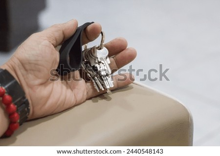 Close up photo of a man's hand holding a set of keys with a black strap on the armrest of a sofa