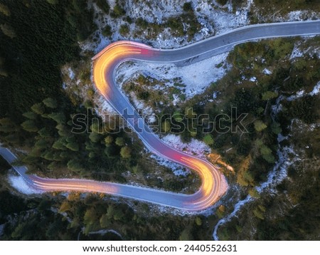 A perpendicular, unusual view of a winding road with traces of passing car lights. Long-Exposure Photography. Yellow and red lines, evening view, mountain road in the Dolomites. 