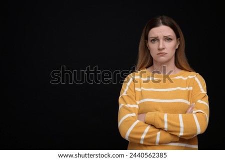 Portrait of sad woman with crossed arms on black background, space for text