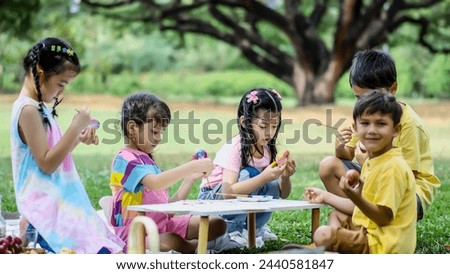 Happy group children in park, cute Asian girl and boy with mix race friend, paint egg with paintbrush together on green grass in garden. Kids celebrate Easter holiday outdoor Royalty-Free Stock Photo #2440581847