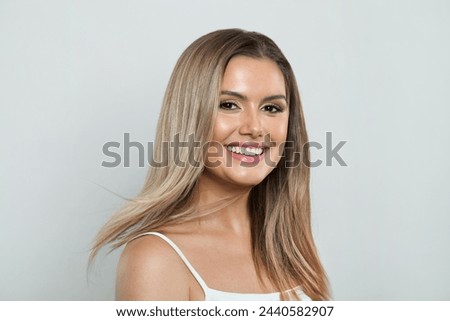 Happy model woman with fresh clear skin and long healthy blonde hair smiling on white background. Facial treatment, hair care and cosmetology concept