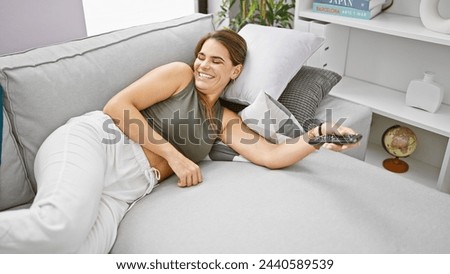 Young beautiful hispanic woman watching tv lying on sofa at home