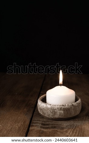 One lit candle stands on a wooden table on a dark background