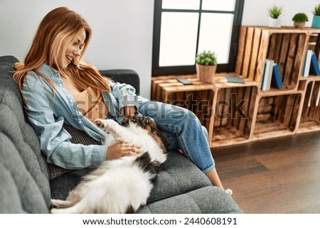 Young caucasian woman sitting on sofa playing with dog at home