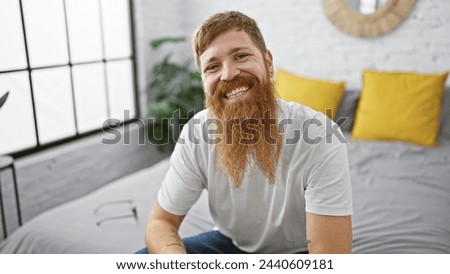 Wake up to a charming morning with a young, happy redhead man, sitting comfortably in bed, smiling confidently in his cozy bedroom, enjoying a relaxing moment of home comfort. Royalty-Free Stock Photo #2440609181