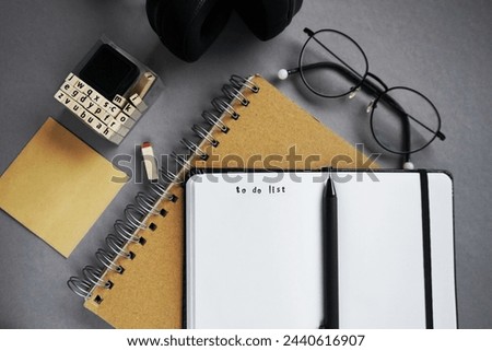 Notepads next to pen, sticky notes, glasses, smartphone and headphones on gray background