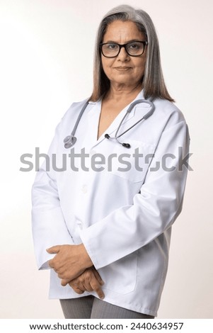 Portrait of smiling confident senior female doctor wearing lab coat standing against white background