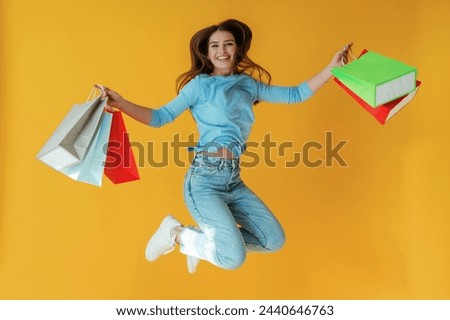Colorful shopping bags in hands. Young woman is against yellow background.
