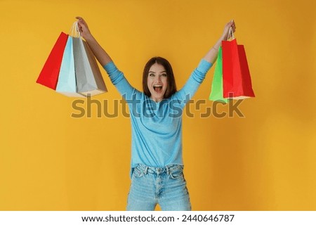 Shopping day, holding bags. Young woman is against yellow background.
