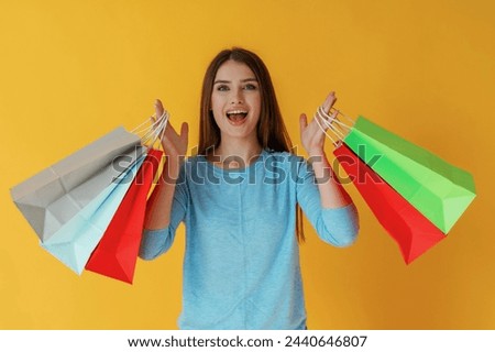 Happy facial expression, with shopping bags. Young woman is against yellow background.