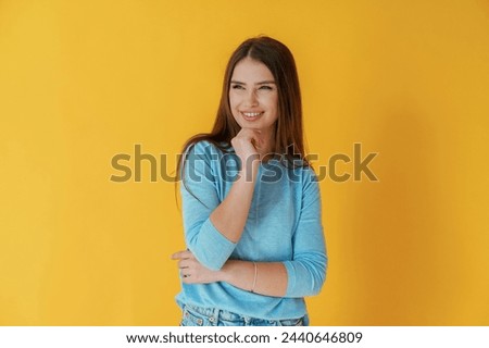 Having bad evil thoughts, smiling of joy. Young woman is against yellow background.