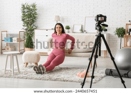 Female sports blogger training on sofa while recording video at home