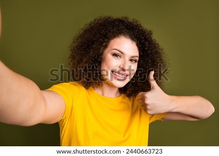 Self portrait of young curly haired lady in yellow t shirt showing thumb up approved for marathon isolated on khaki color background