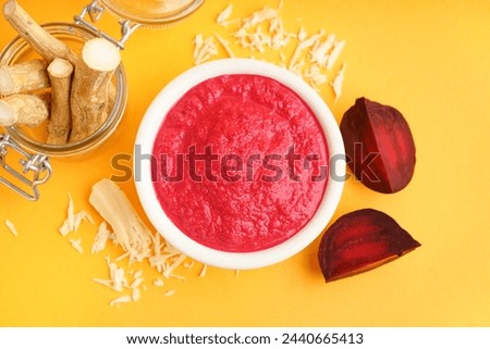 Horseradish sauce with beet in bowl and pieces of beet on yellow background. Top view