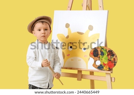 Cute little artist with drawing of giraffe on yellow background