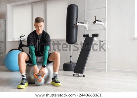 Sporty young man with kettlebell on fitball at gym
