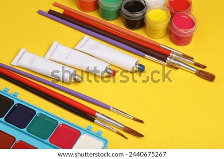 Set of paints, colored pencils and brushes on a yellow background. Products for creativity