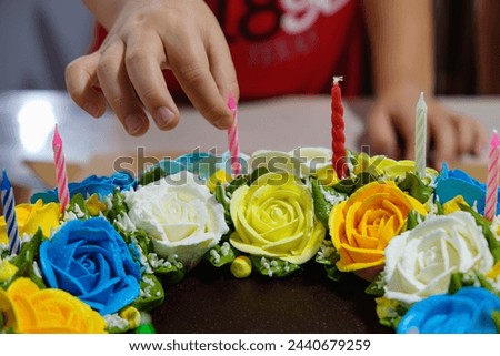 Little kid put the candles on top 
 of Birthday Cake with beautiful colorful flower cake decoration. Close up photo.