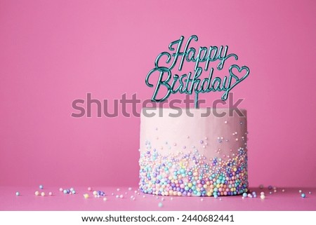 Celebration birthday cake with happy birthday cake pick against a pink background