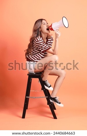 The young Asian woman in casual clothes with gesture of siting isolated on the orange background 
