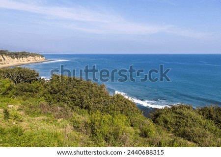 a beautiful spring landscape at Point Dume beach with blue ocean water, lush green trees and plants, homes along the cliffs, waves, blue sky and clouds in Malibu California USA Royalty-Free Stock Photo #2440688315