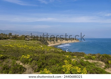 a beautiful spring landscape at Point Dume beach with blue ocean water, lush green trees and plants, homes along the cliffs, waves, blue sky and clouds in Malibu California USA Royalty-Free Stock Photo #2440688321