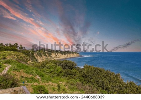 a beautiful spring landscape at Point Dume beach with blue ocean water, lush green trees and plants, homes along the cliffs, waves, blue sky and clouds in Malibu California USA Royalty-Free Stock Photo #2440688339