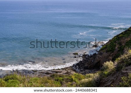 waves rolling into the shore over the rocks with lush green trees and plants and people on the rocks at Point Dume Beach in Malibu California USA Royalty-Free Stock Photo #2440688341