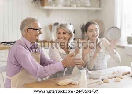 Multi-generational family laughing, having fun, joking, cooking together, clap hands, enjoy cooking process, make homemade dough for holiday pastries spend weekend time together in modern cozy kitchen Royalty-Free Stock Photo #2440691489