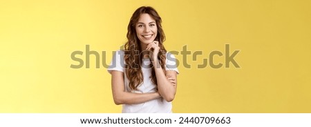Tender feminine enthusiastic charming european woman curly long hairstyle laughing silly gaze grinning joyfully touch chin intrigued standing curious interested listening amused yellow background. Royalty-Free Stock Photo #2440709663