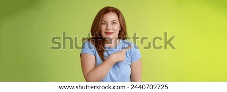 Surprised excited middle-aged wondered redhead woman pointing left amused standing thrilled joyful green background look camera curious interested cannot wait check-out great promo. Royalty-Free Stock Photo #2440709725