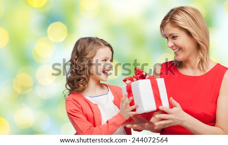 people, holidays, christmas and family concept - happy mother and daughter giving and receiving gift box over green lights background