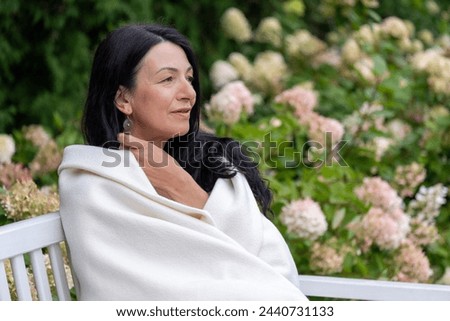 A mature woman, wrapped warmly, gazes into the distance, her expression one of peaceful self-acceptance during the life transition of midlife. High quality photo