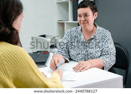 Individual approach: a middle-aged, brunette girl with a short haircut sits next to the client and provides a personalized solution, taking into account their needs. Royalty-Free Stock Photo #2440788127